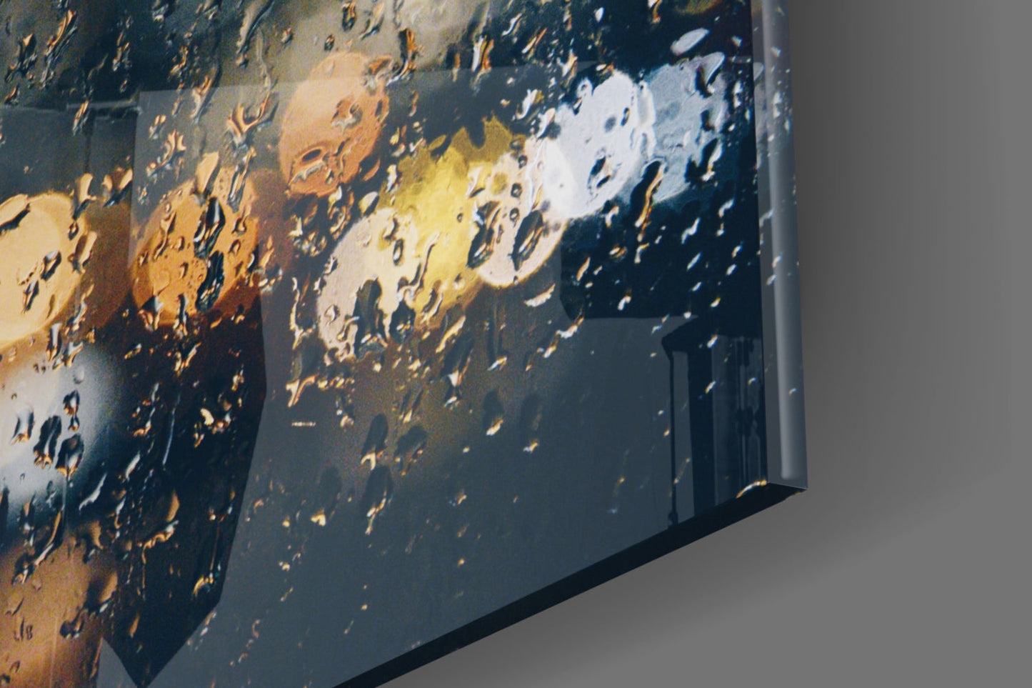 Close-up angled view of rain glass wall art with water droplets and warm golden light reflections on dark surface.