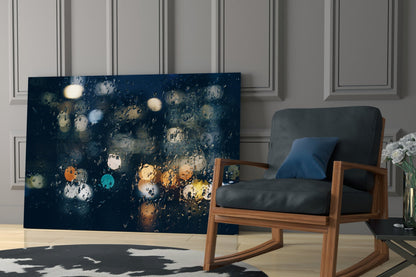 Rain Glass Wall Art displayed leaning against wall beside wooden chair, showing dark blue surface with colorful water droplets and bokeh lights.