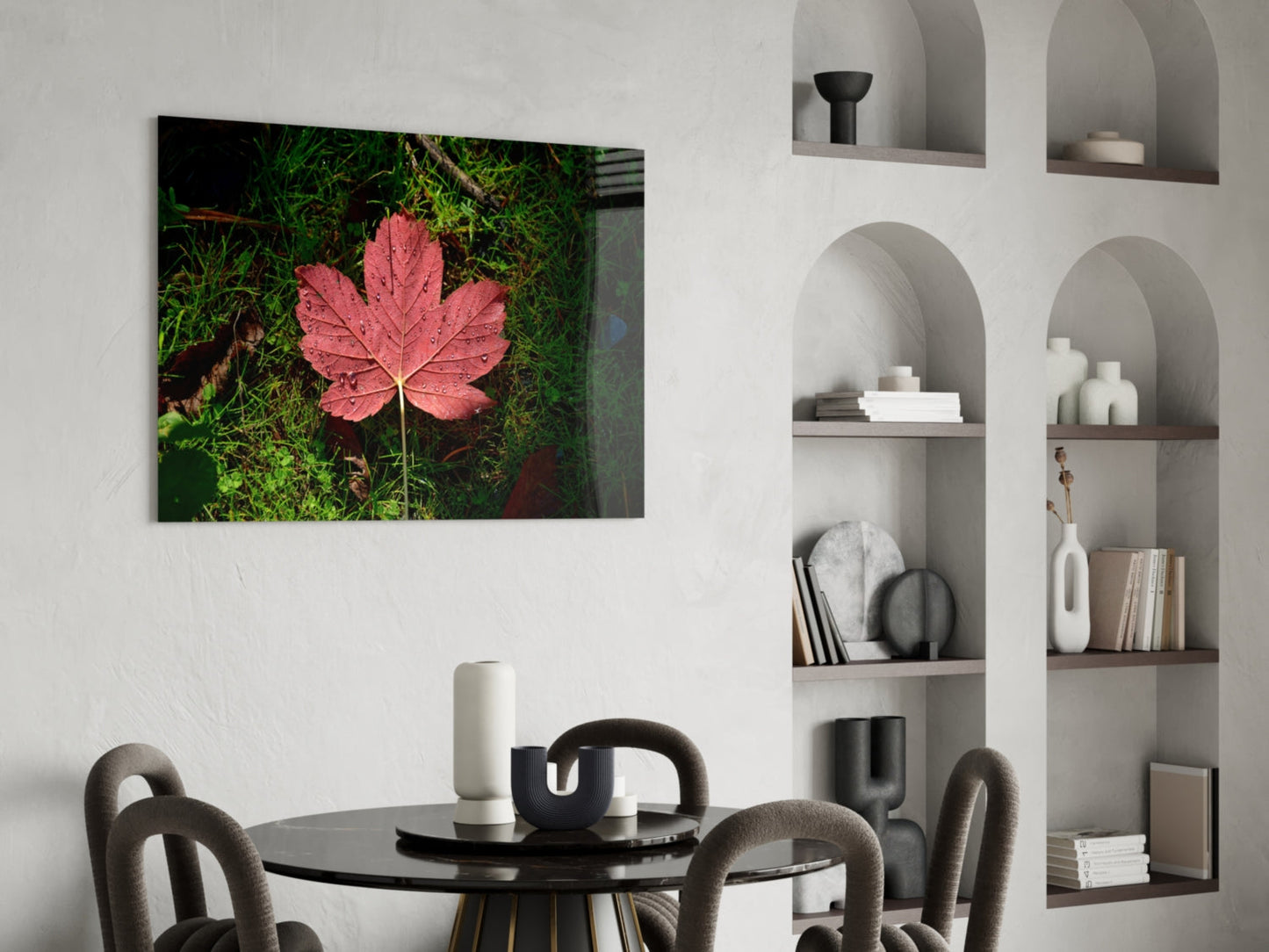 Pink maple leaf glass wall art displayed above a black dining table in a modern white interior with built-in shelving.