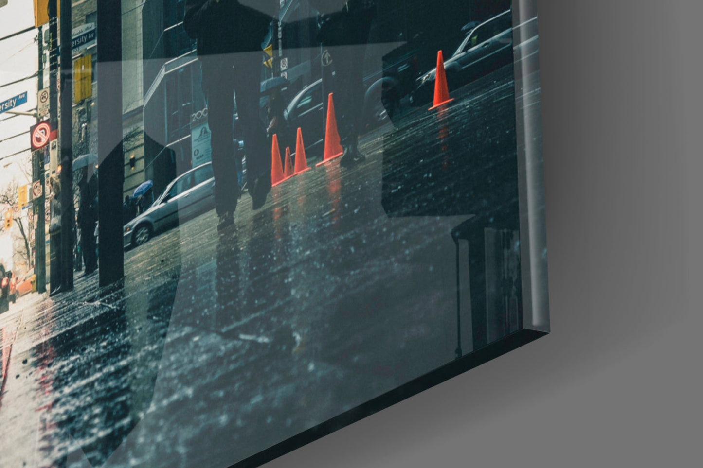 Angled side view of glass wall art displaying a wet urban street with parked cars and red traffic cones.