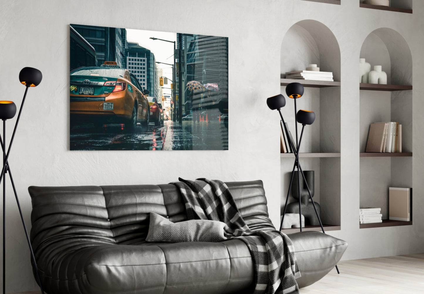 Modern living room with black leather sofa, glass wall art depicting yellow taxi on rainy city street mounted above.