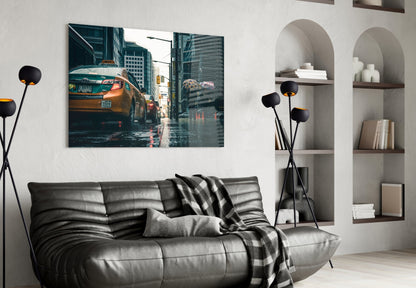 Modern living room with black leather sofa, glass wall art depicting yellow taxi on rainy city street mounted above.