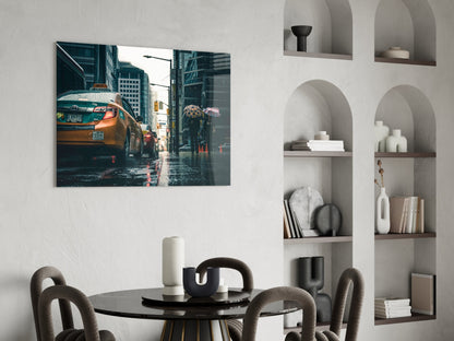 Glass wall art depicting a wet city street with yellow taxi cabs and tall buildings, displayed above a black dining table.