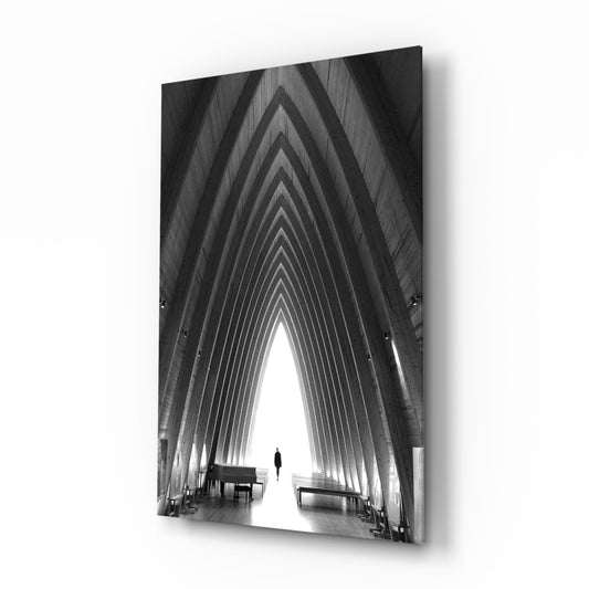 Black and white photograph of a symmetrical arched corridor with a solitary figure centered in bright light, displayed as a framed glass wall art piece.