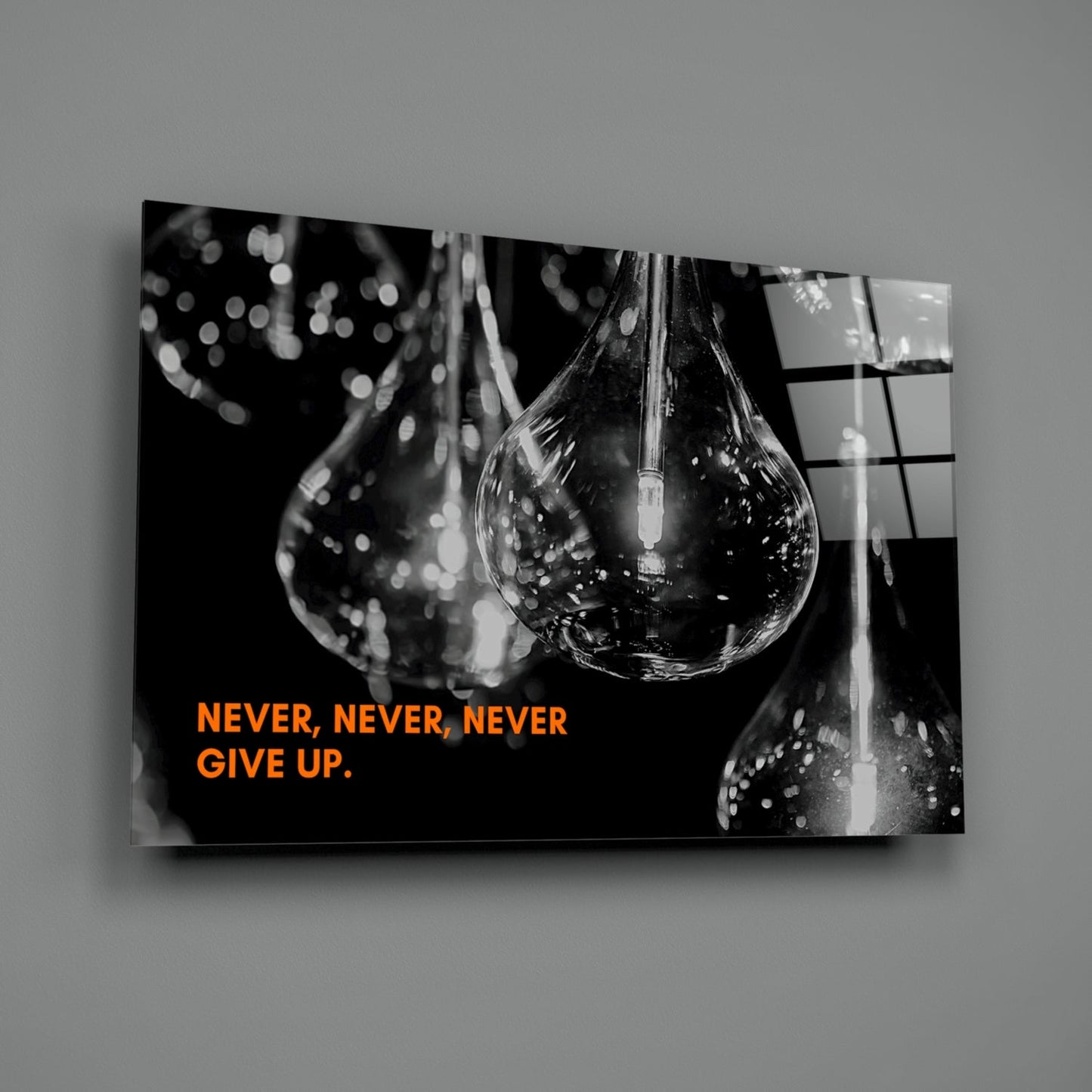 Black and white glass wall art displaying water droplets with orange text reading "NEVER, NEVER, NEVER GIVE UP" against dark background.