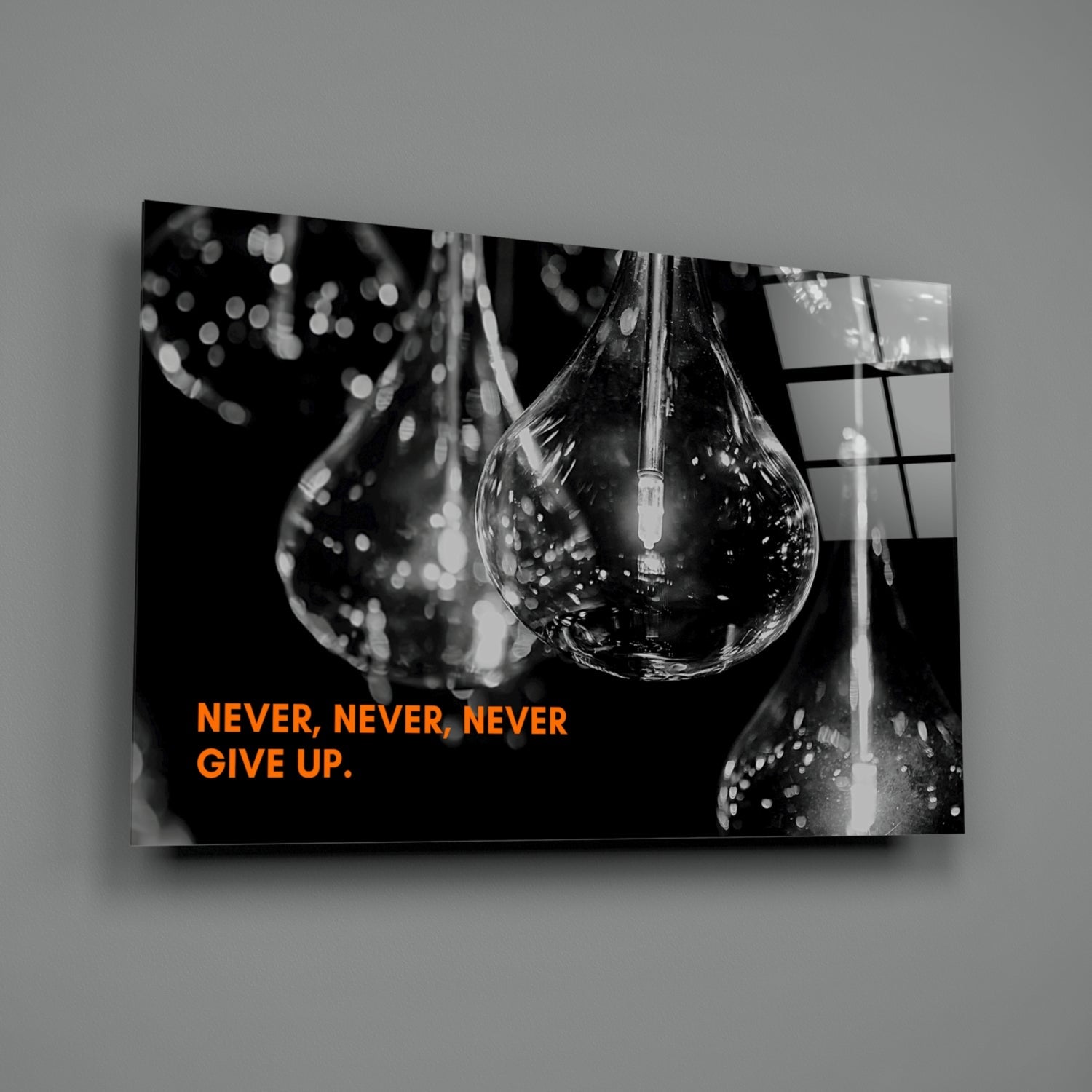 Black and white glass wall art displaying water droplets with orange text reading "NEVER, NEVER, NEVER GIVE UP" against dark background.