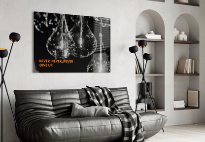 Black and white motivational canvas with orange "Never, Never, Never Give Up" text displayed above gray leather sofa in modern living room.