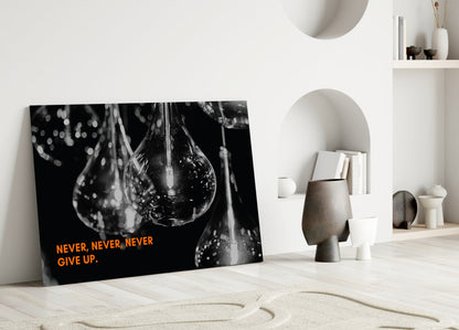 Black and white glass wall art with water droplet imagery and orange "Never, Never, Never Give Up" text, displayed in minimalist white interior setting.