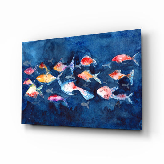 Angled view of glass wall art featuring colorful watercolor fish swimming on deep blue background, displayed at perspective angle showing glass thickness and shadow.