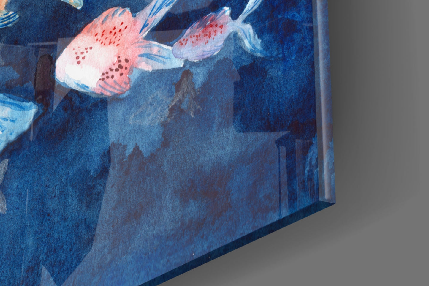 Close-up angled view of glass art showing red and white fish with spotted patterns swimming in deep blue water against gray background.