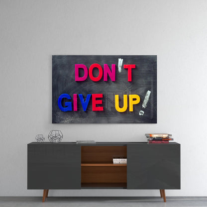 Motivational glass wall art with colorful letters spelling "DON'T GIVE UP!" mounted above a mid-century modern console table in a minimalist interior setting.
