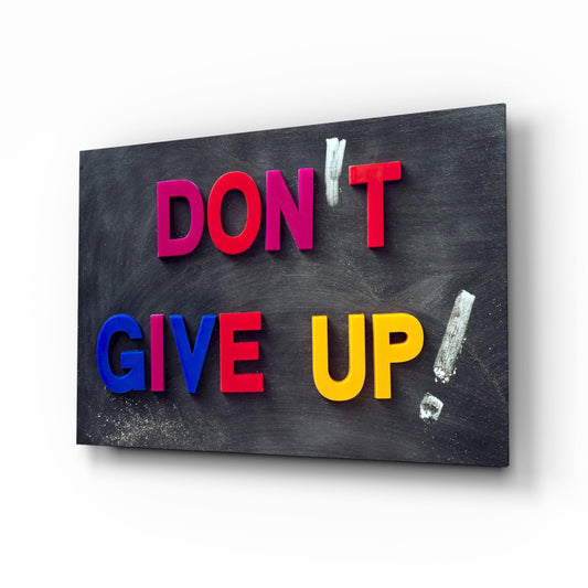 Colorful 3D letters spelling "DON'T GIVE UP" mounted on a dark chalkboard surface with white chalk marks.