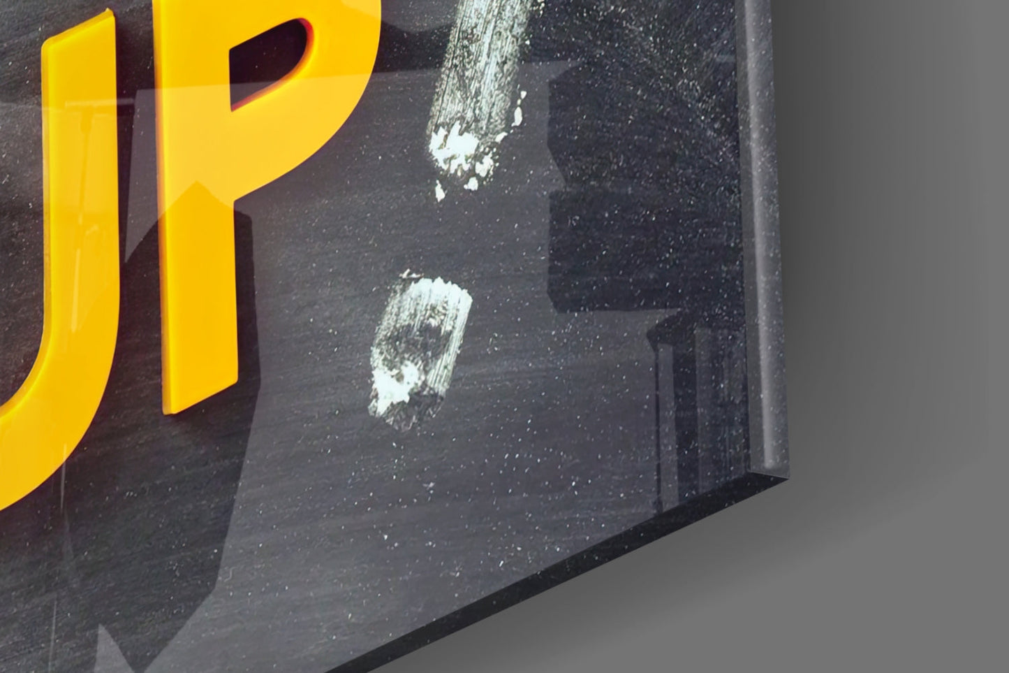 Close-up of black glass wall art with yellow "P" letter and white paint splatters visible on surface.