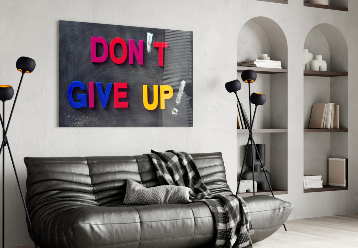 Colorful "Don't Give Up" glass wall art in pink, blue, and yellow text displayed above a black leather sofa in a modern living room interior.