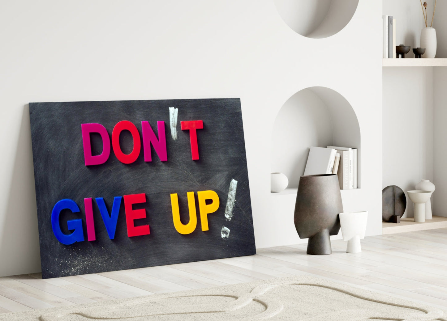 Motivational glass wall art with colorful 3D letters spelling "DON'T GIVE UP" on dark chalkboard background, displayed in minimalist white interior setting.