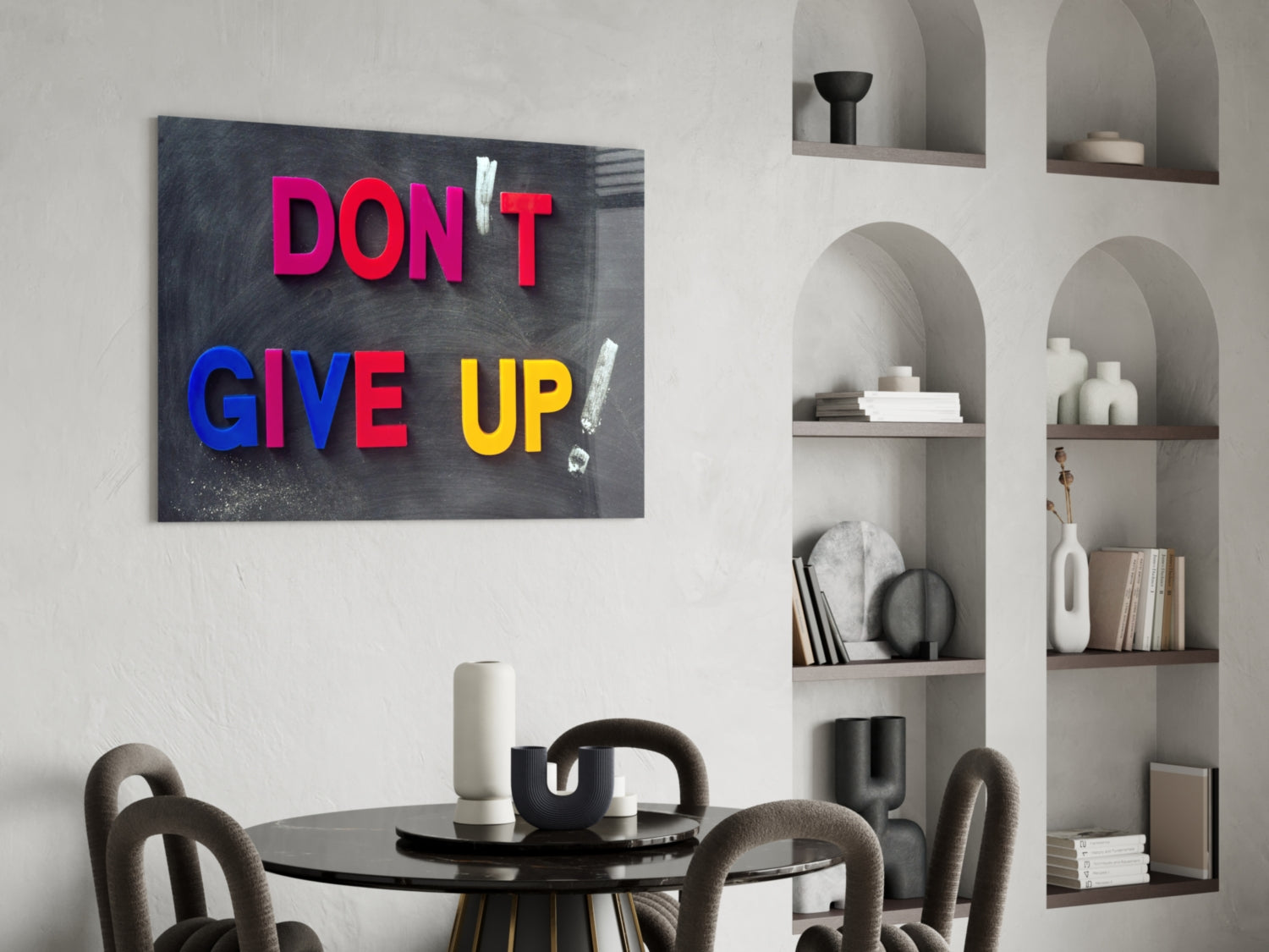Motivational glass wall art with colorful "DON'T GIVE UP" text displayed above a round black table and shelving unit in a modern interior setting.
