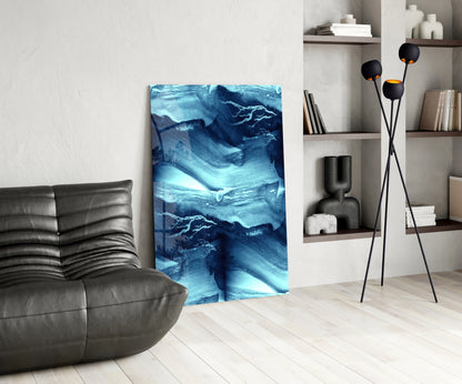 Blue Serenity Glass Wall Art displayed in a modern living room beside a gray leather chair and black floor lamp with shelving.
