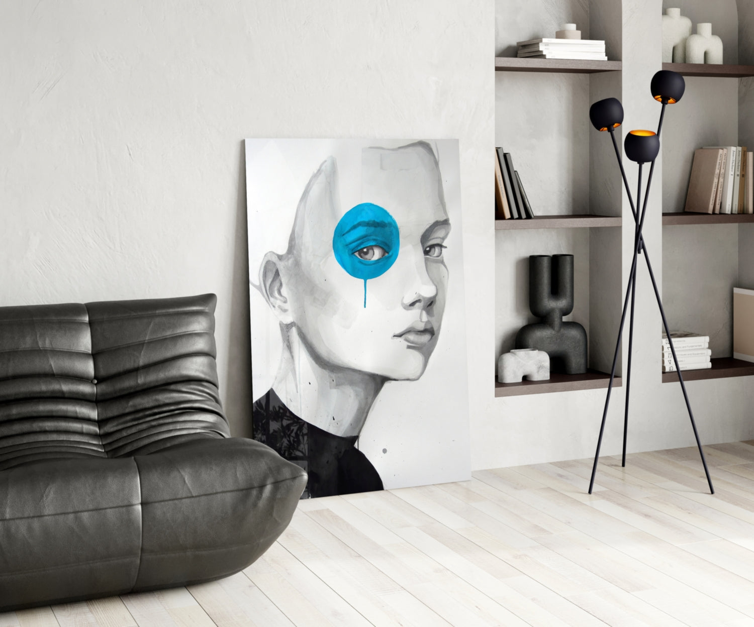 Modern living room featuring glass wall art of a monochrome face with bright blue circular eye detail, displayed next to black leather chair and shelving.
