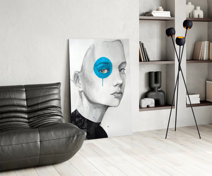 Modern living room featuring glass wall art of a monochrome face with bright blue circular eye detail, displayed next to black leather chair and shelving.