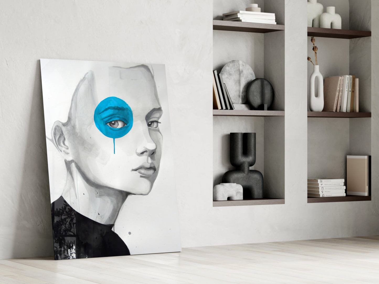 Modern minimalist interior with framed portrait artwork featuring pencil sketch face and bright blue circular eye design leaning against white wall beside shelving unit.