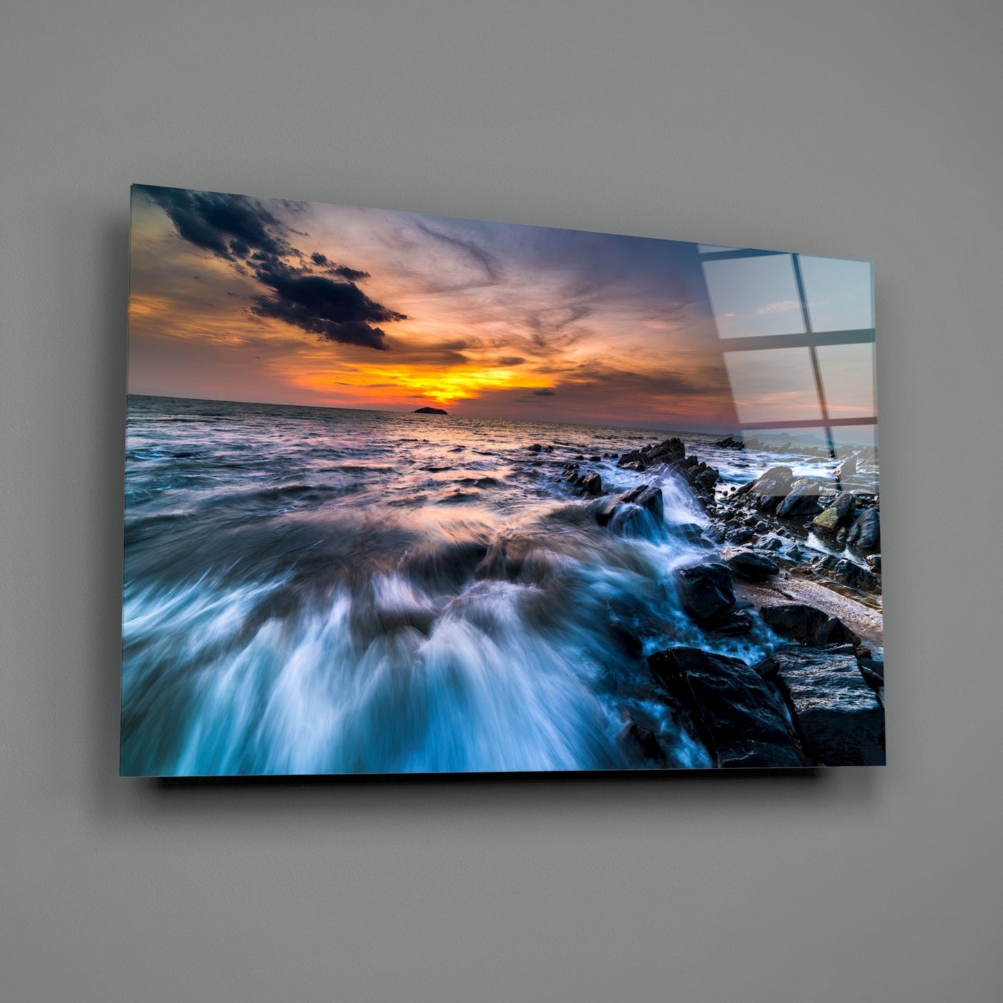Coastal sunset glass wall art mounted on gray wall showing rocky shoreline, waves, and orange sky with grid pattern overlay.