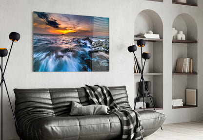 Endless Sea glass wall art depicting a rocky coastline with golden sunset and blue waves displayed above a gray sofa in a modern living room.