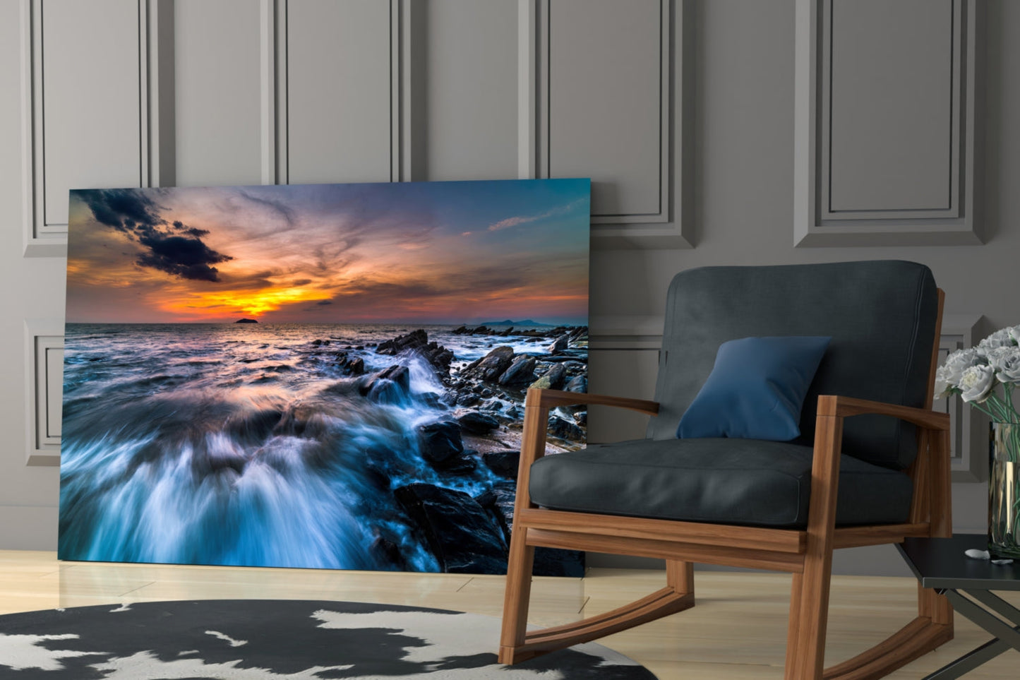 Endless Sea glass wall art depicting a dramatic coastal sunset with rocky shoreline and waves, displayed in a modern living room beside a wooden chair.