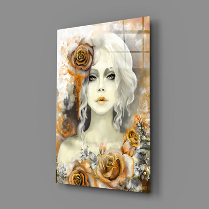 Glass wall art panel displaying a pale-faced woman with wavy white hair adorned with golden roses, surrounded by watercolor floral elements in amber and cream tones.