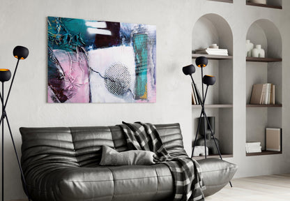 Abstract glass wall art with teal, pink, and white tones featuring branches and geometric patterns, displayed above a black leather sofa in a modern living room.