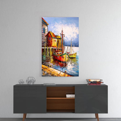 Glass wall art depicting colorful fishing boats docked at a seaside village with red and yellow buildings and snow-capped mountains, displayed above a mid-century modern console table.
