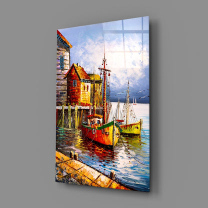 Colorful glass wall art panel displaying sailboats and waterfront cottages in vibrant reds, yellows, and blues, shown at an angle against gray background.