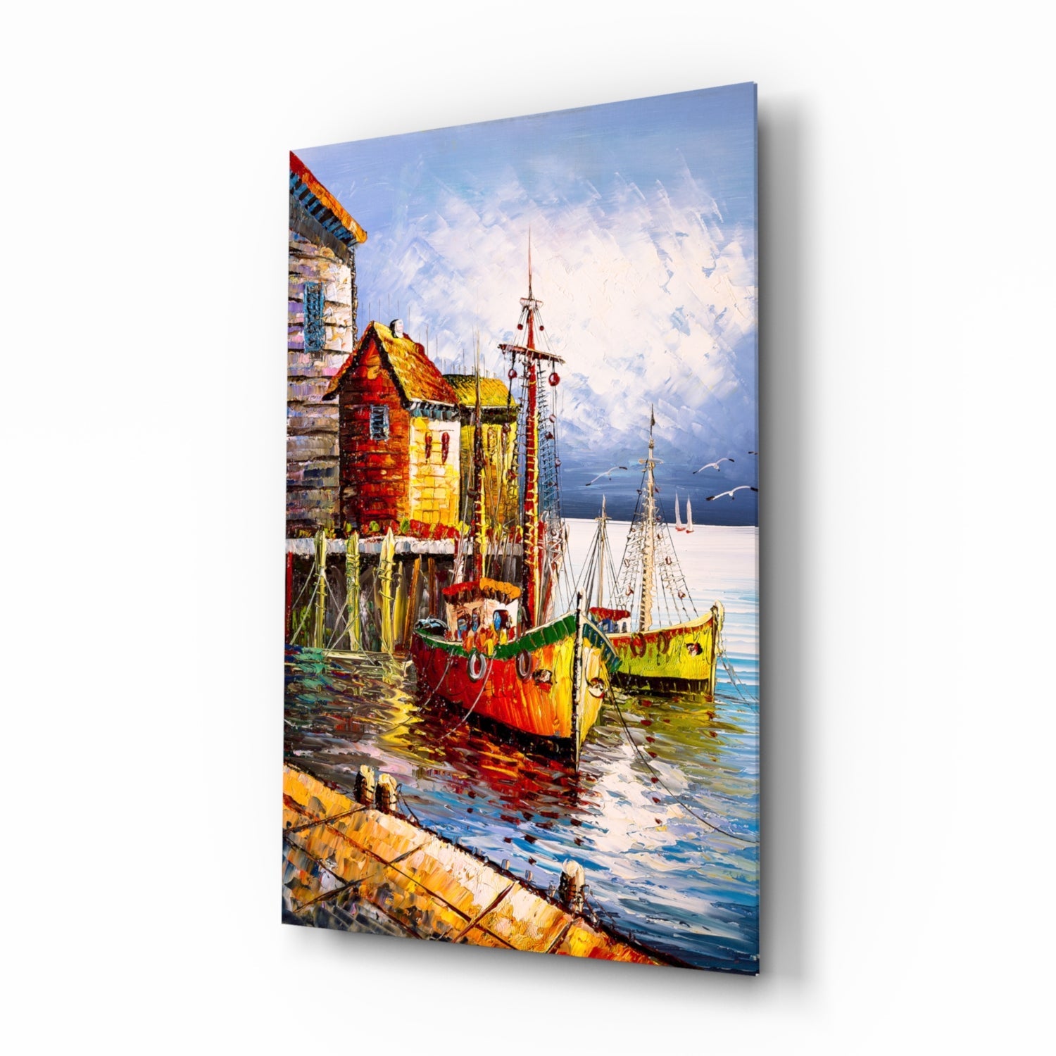 Colorful glass wall art depicting red and yellow fishing boats moored at a wooden dock with seaside buildings and sailboats in the background.