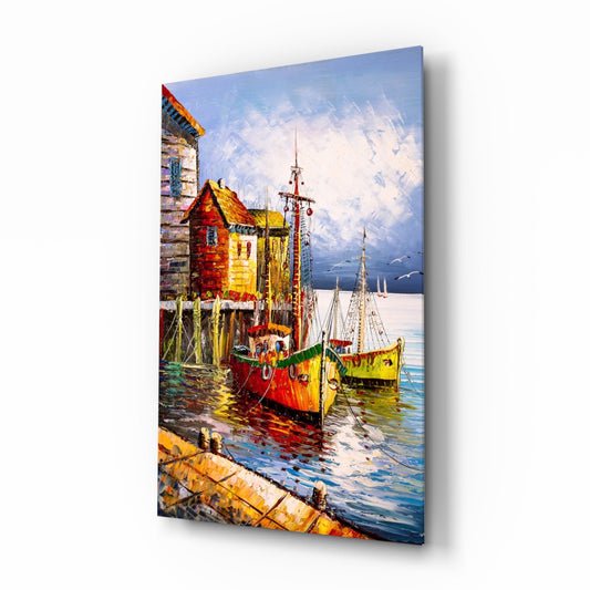 Colorful glass wall art depicting red and yellow fishing boats moored at a wooden dock with seaside buildings and sailboats in the background.
