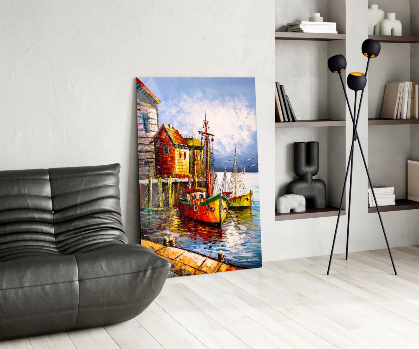 Colorful glass wall art depicting red and yellow boats docked at a waterfront building, displayed in a modern living room with black leather furniture and white shelving.
