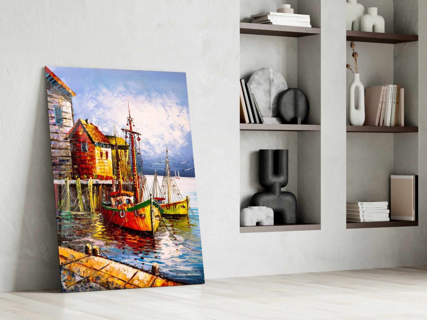 Colorful glass wall art depicting red and yellow fishing boats at a dock, displayed leaning against a white wall next to built-in shelving.