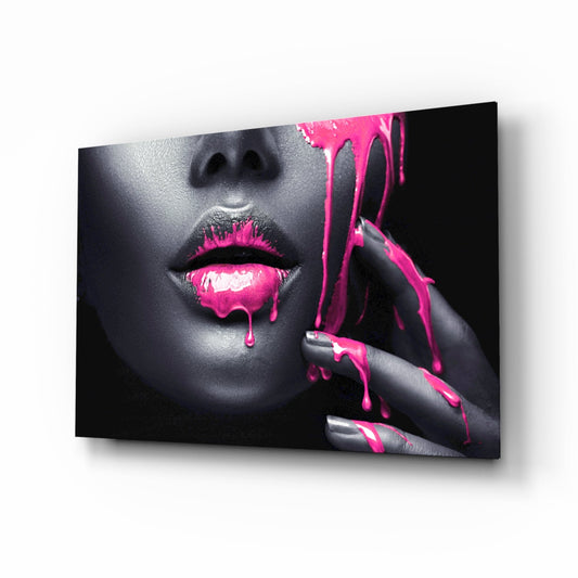 A angled product view of a glass wall art panel displaying a woman's face with bright pink paint dripping from her lips and hand against a dark background.