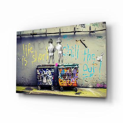 Street art mural on concrete wall showing two nude figures above graffitied trash bins with yellow and blue text reading "life is short" and "chill the out.