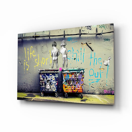 Street art mural on concrete wall showing two nude figures above graffitied trash bins with yellow and blue text reading "life is short" and "chill the out.