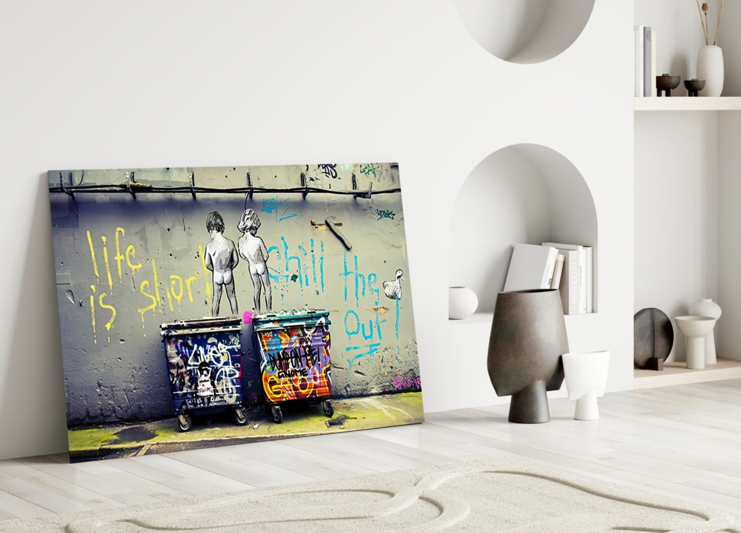 Street art glass wall art leaning against white wall displays two children, trash cans, and yellow and blue text.