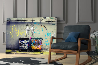 Glass wall art displaying graffiti-style street art with two figures, colorful trash cans, and yellow and blue text reading "life is short" and "chill the out," mounted in modern room setting.
