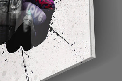 Close-up of white speckled glass wall art showing black ink splatter detail and edge profile against gray background.