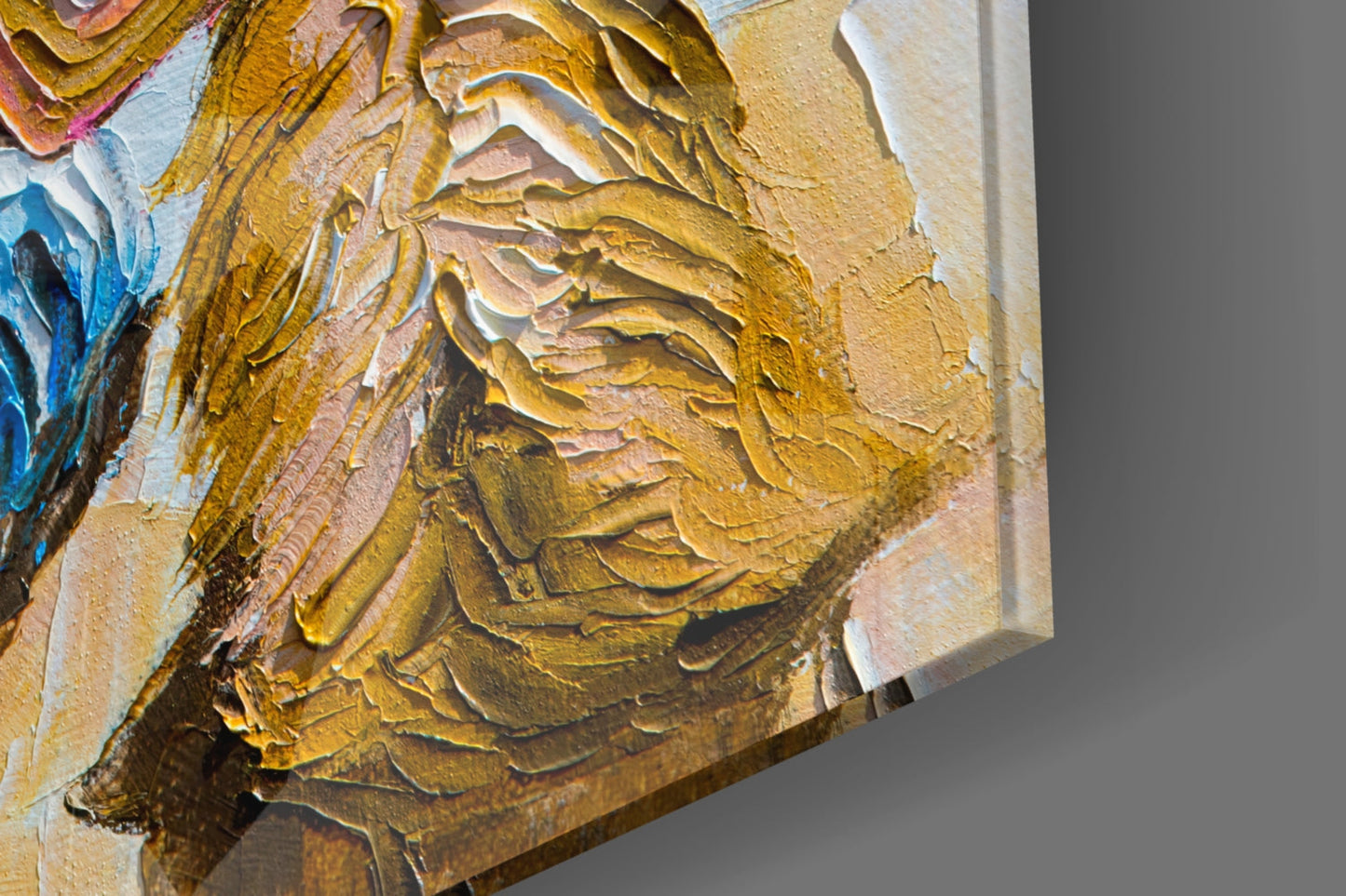 Close-up of textured glass wall art showing impasto brushstrokes in golden, ochre, and cream tones with blue accents, angled view highlighting dimensional surface.