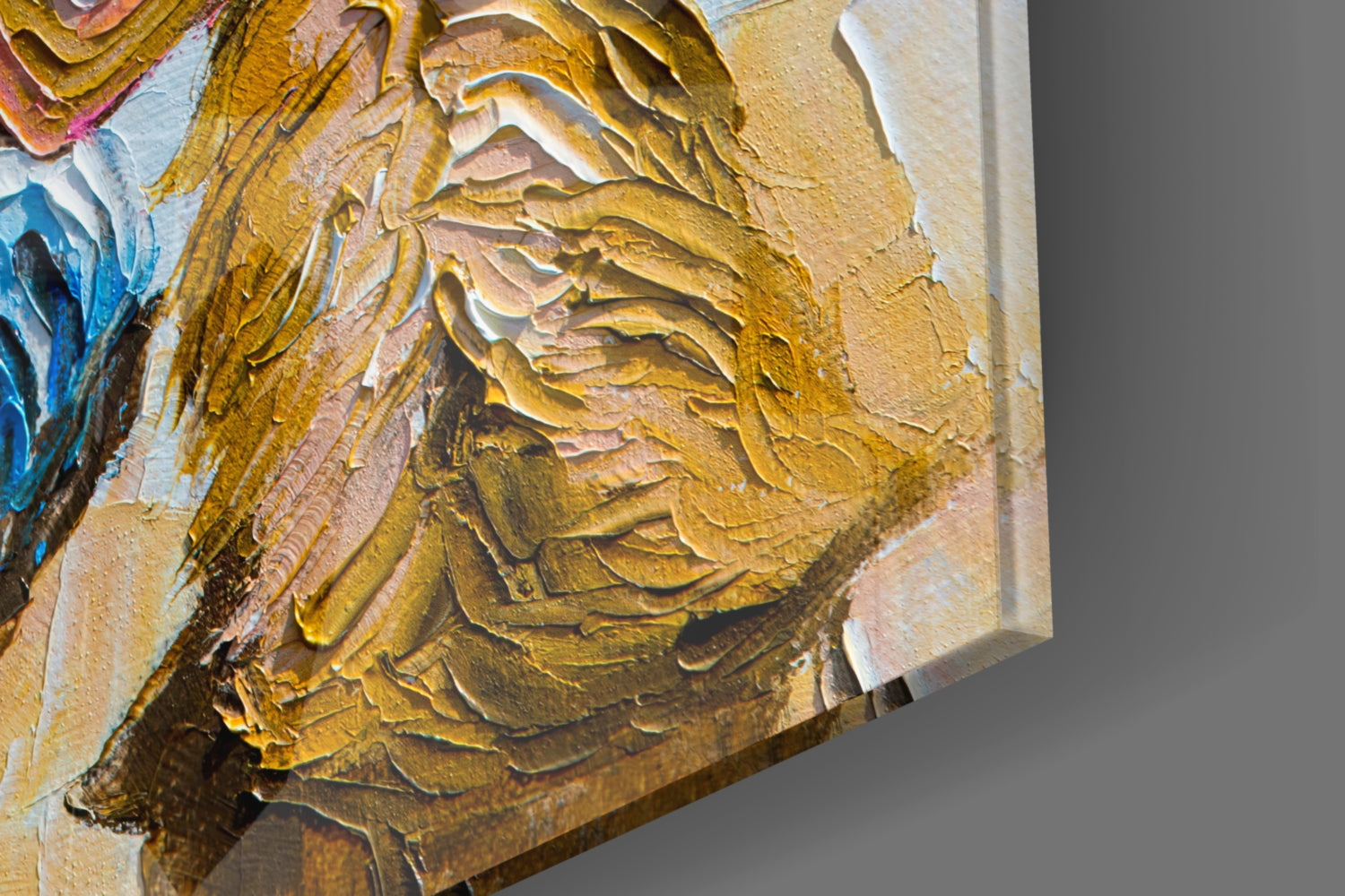 Close-up of textured glass wall art showing impasto brushstrokes in golden, ochre, and cream tones with blue accents, angled view highlighting dimensional surface.