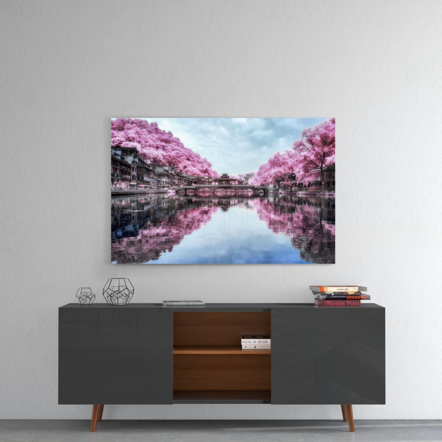 Glass wall art featuring a canal lined with vibrant pink flowering trees reflected in still water, hung above a dark mid-century credenza.