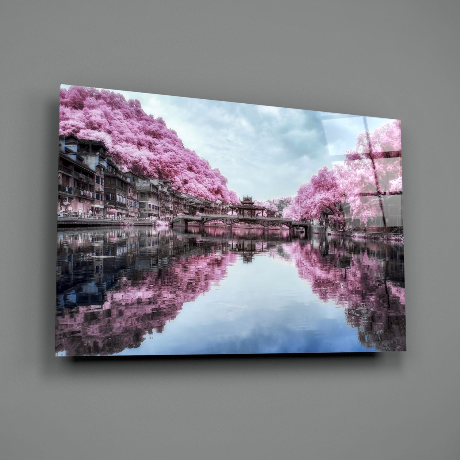 Glass wall art displaying serene canal scene with pink flowering trees reflected in still water and traditional architecture.