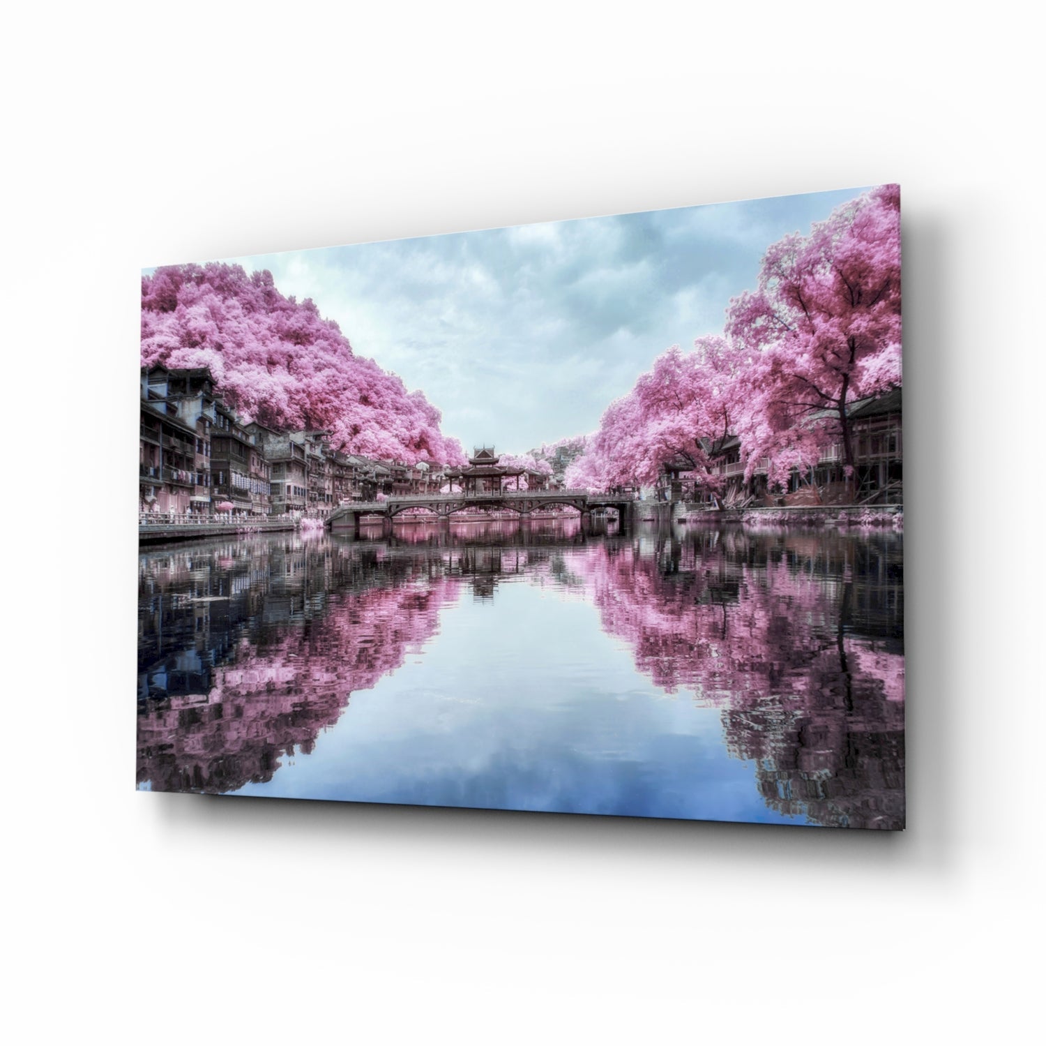 Glass wall art displaying a serene canal scene with pink flowering trees reflected in still water and traditional architecture, shown at an angle.
