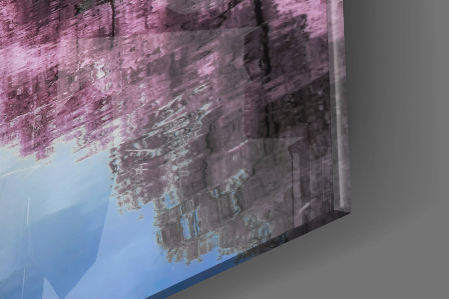Pink landscape glass wall art displayed at an angle, showing inverted mountain reflection on blue sky background.