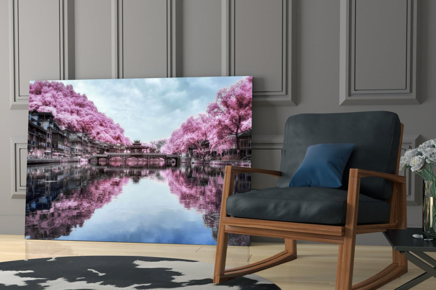 Glass wall art displaying a canal with pink flowering trees and their reflections in still water, displayed in a modern interior with a wooden chair.
