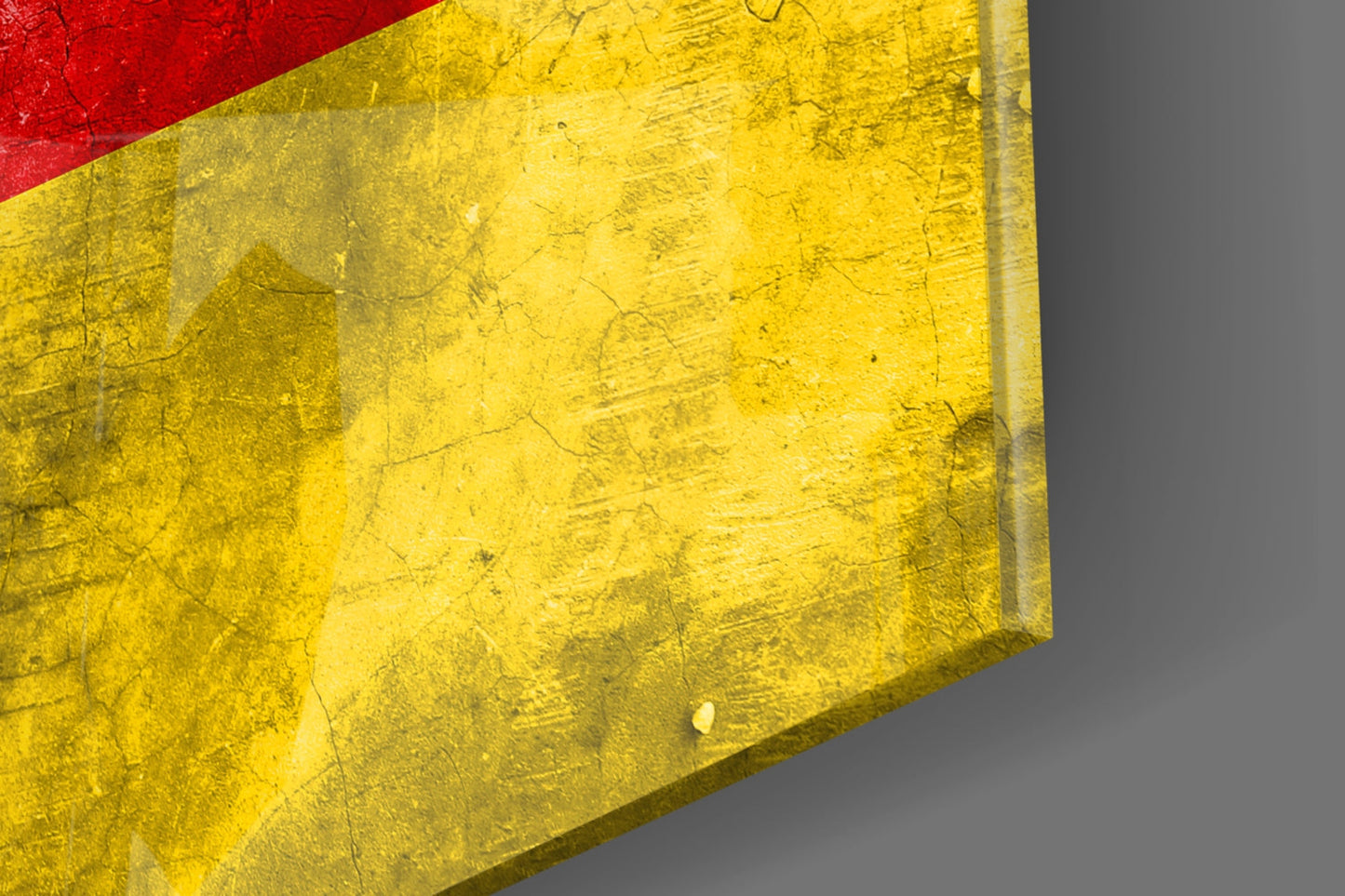 Close-up angled view of German flag glass wall art showing textured yellow section with red stripe, mounted on gray surface.