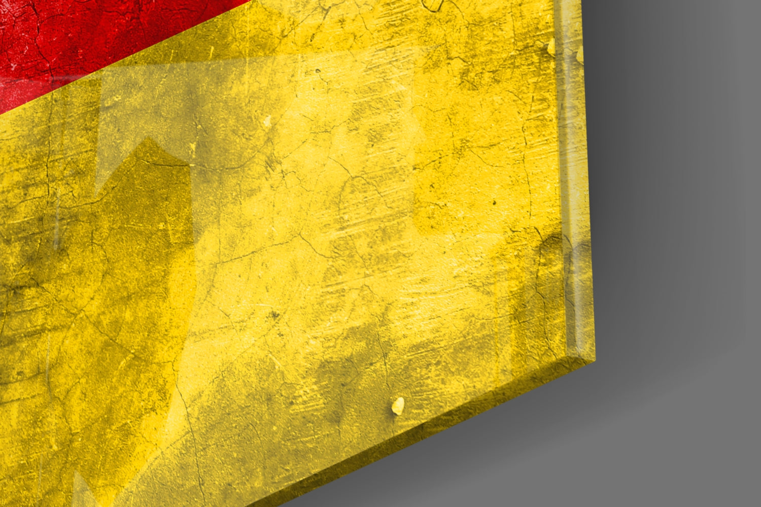 Close-up angled view of German flag glass wall art showing textured yellow section with red stripe, mounted on gray surface.
